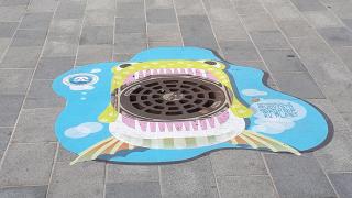 Mahanpuruja muovista - kampanjan tarra hulevesikaivon ritiläkannen ympärillä.