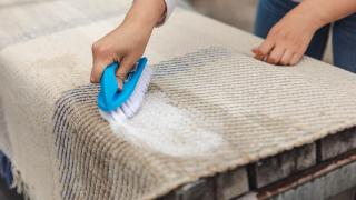 Henkilö pesee maton harjalla.