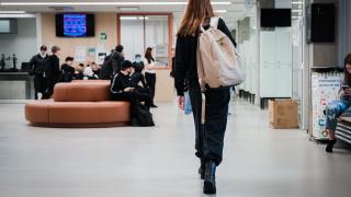 Oppilas kävelee kuvaajasta pois päin reppu selässään koulun käytävällä. Taustalla on muita oppilaita istumassa ja seisomassa.