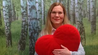 Henkilö jolla on iso punainen pehmosydän sylissä.