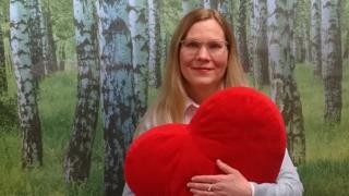 Henkilö jolla on iso punainen pehmosydän sylissä.