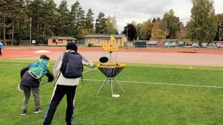 Kaksi lasta heittää frisbeegolfkiekkoja koriin.