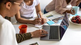 Henkilöitä kannettavan tietokoneen ääressä. 