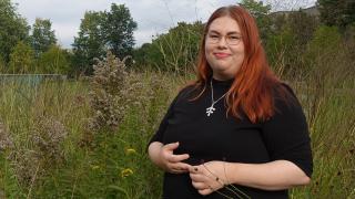 Nainen seisoo korkean heinikon edessä puistossa.