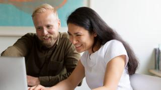 In the picture, two people are smiling while looking at a computer.