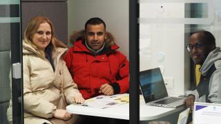 Vantaan monikielisen neuvonnan asiakkaat Tetiana ja Abbas ovat neuvontakopissa monikielisen neuvojan Abdishakurin kanssa. Kaikki katsovat kameraan.