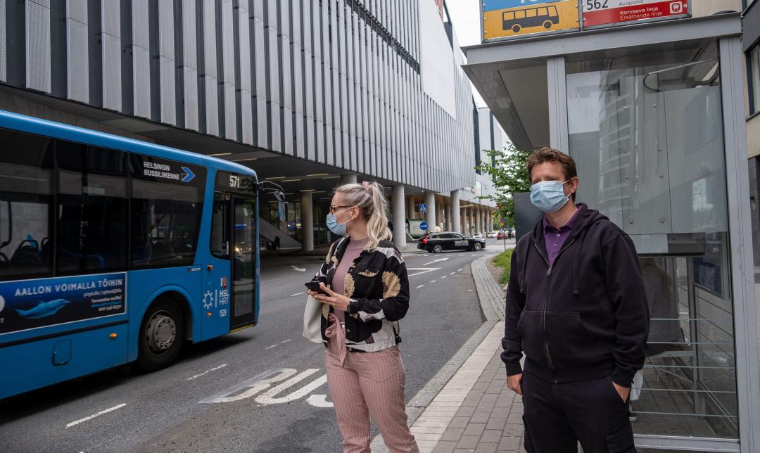 Kaksi ihmistä odottamassa bussia pysäkillä Tikkurilan rautatieaseman edessä.