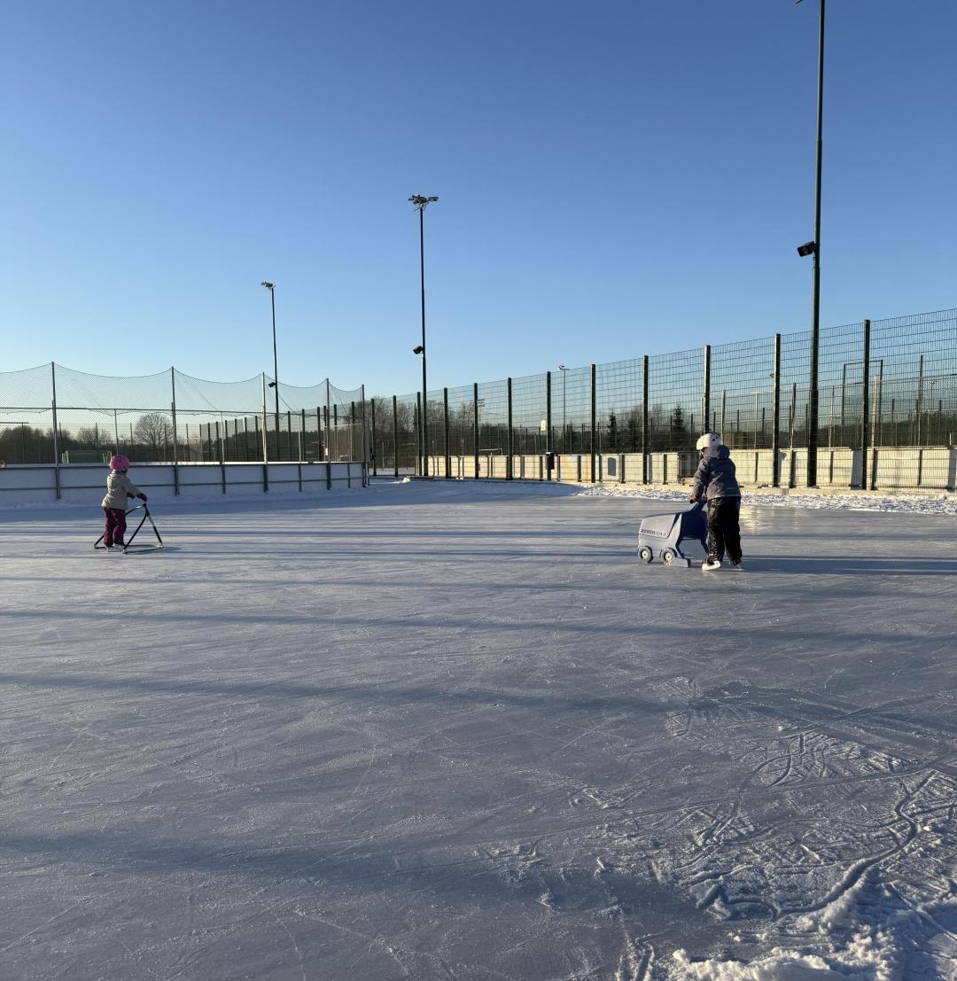 Kartanonkosken tekojääkentällä lapsia luistelemassa käyttäen luistelutukia.
