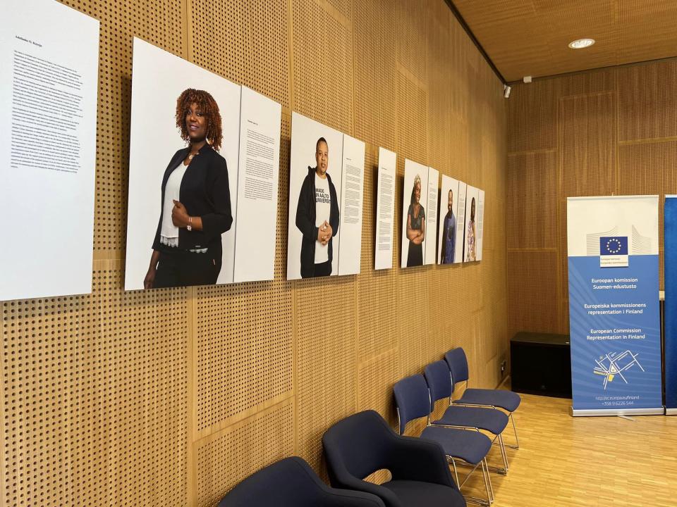 Valukuvanäyttelyn kuvia teksteineen vasemmalla, puunvärisellä seinällä. Teosten alla tuolirivi.
