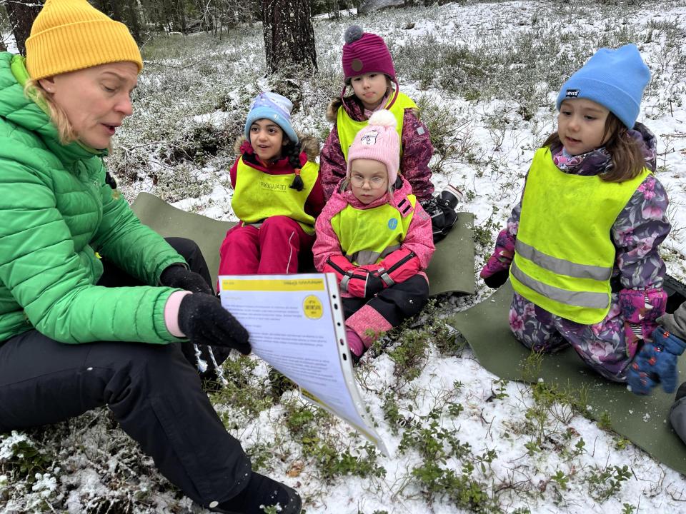 Opettaja lukee päiväkodin metsäryhmälle kirjettä. Lapset istuvat mättäällä.