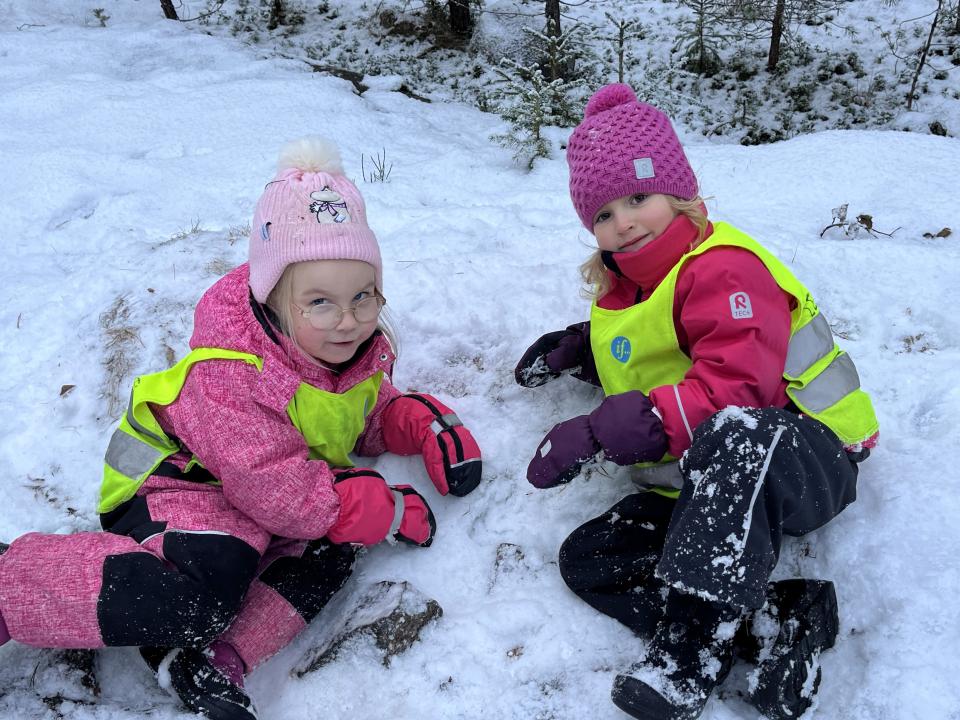 Kaksi lasta makoilee lumihangessa ja hymyilee kameralle.