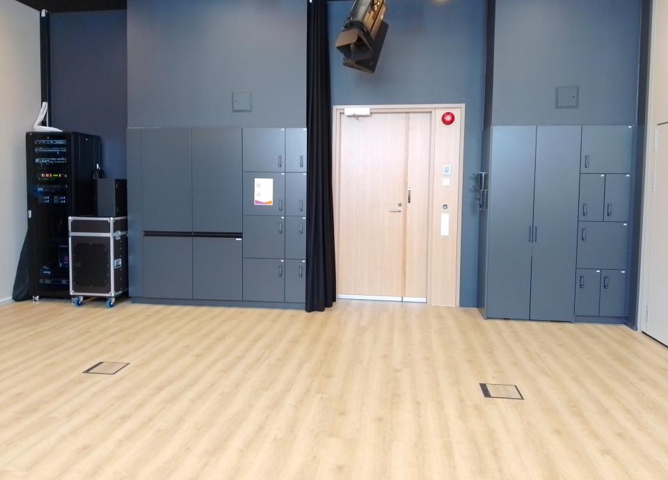 Tyhjätila, jossa vaalea lattia. Tilan perällä tumma seinä, jossa ovi ja mustia kaappeja.