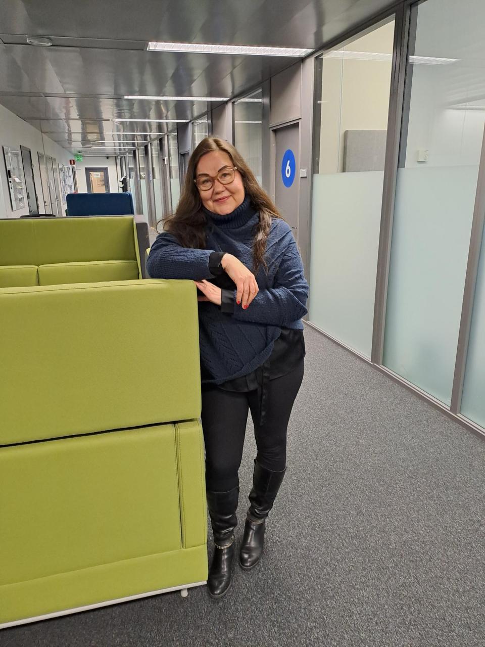 Sari Latvasalo nojaa tasoon ja hymyilee kameralle Vantaan Vernissakadun työllisyyden ja kotoutumispalveluiden tiloissa.