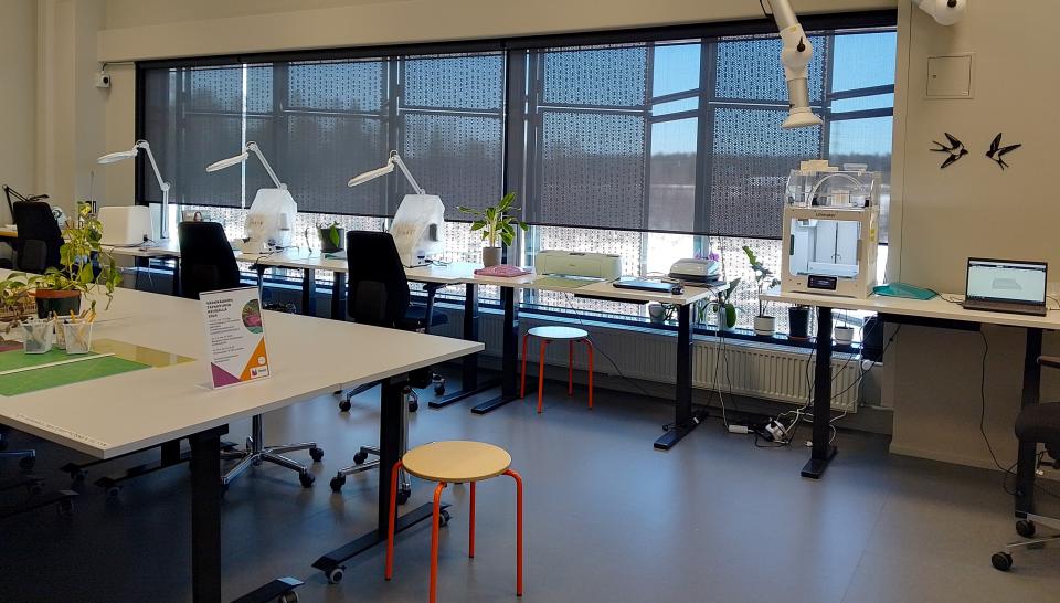 Työtila, jossa pöydillä laitteita kuten ompelukone ja 3D-printteri. 