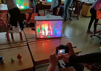 Kytöpuiston koulun valotaidetyöpajan taideteos pöydällä. Ympärillä seisoo ihmisiä.